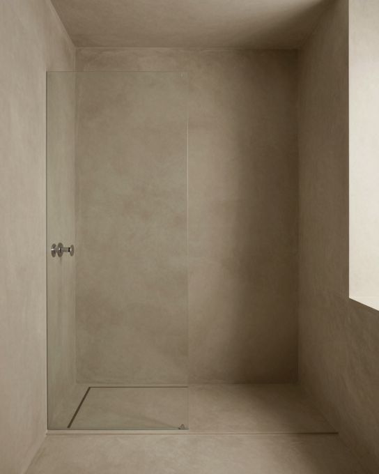 Illustration: a microcement shower and bathroom in warm greige, seamless walls and floor with no grout lines, a linear drain